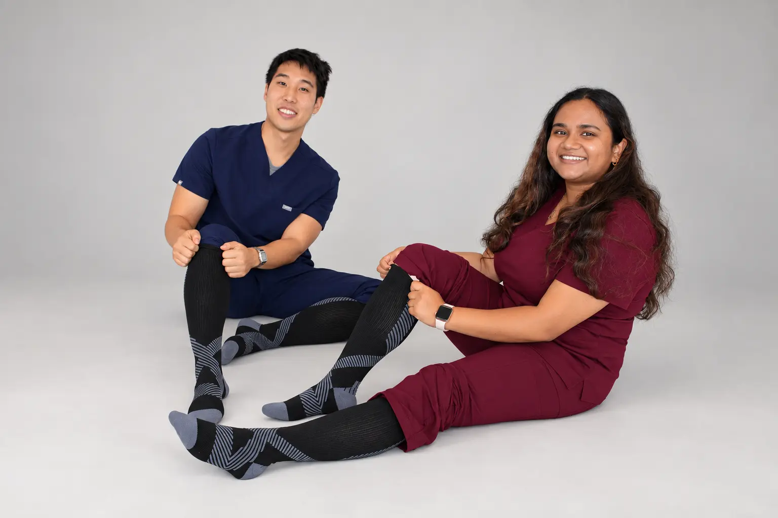 Two nurses in scrubs sitting on the floor wearing NursingRx compression socks